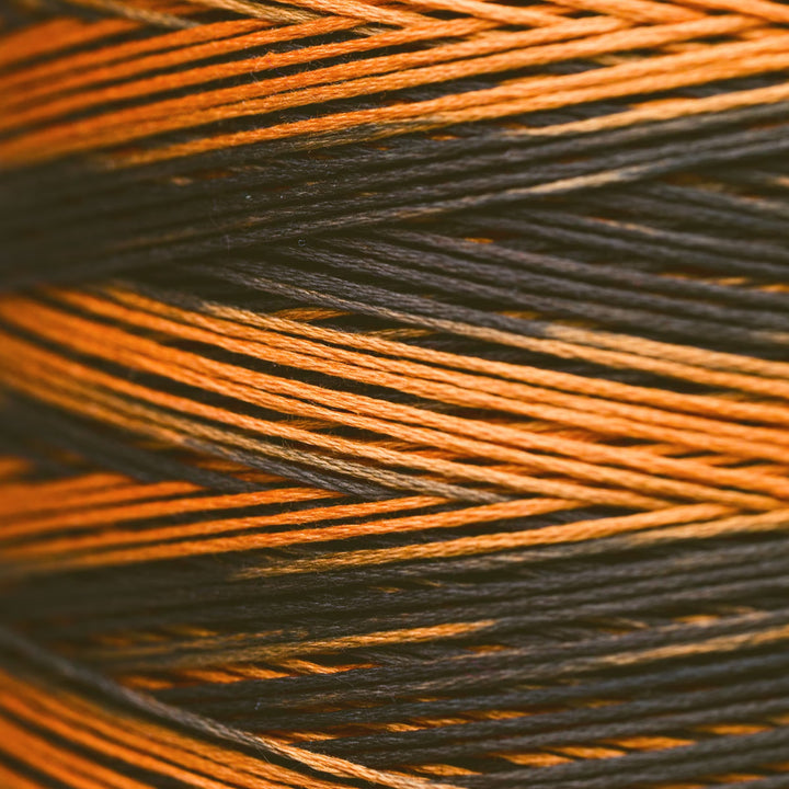 Close-up of tightly wound thread strands in alternating orange and black colors, filling the entire frame.