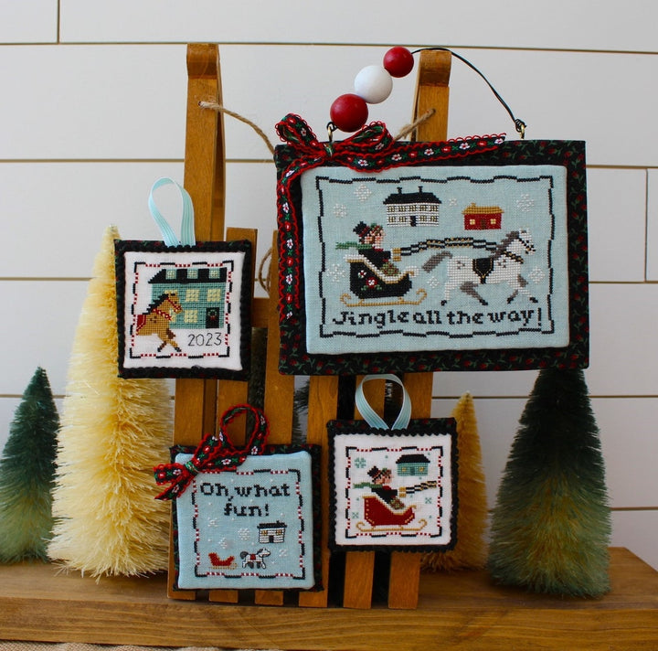 Set of cross-stitched Christmas ornaments on a wooden stand with decorative trees.
