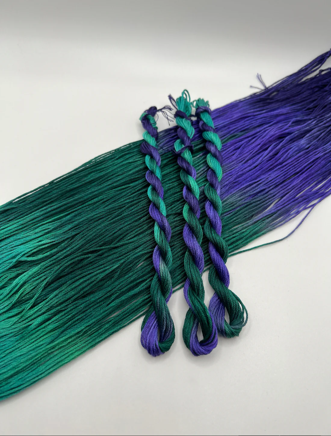 Two twisted skeins of green and purple thread on a white background