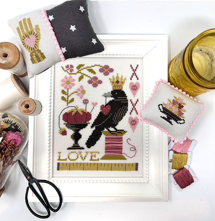 Cross-stitched design with a crow, flowers, and the word 'LOVE' on a white background.