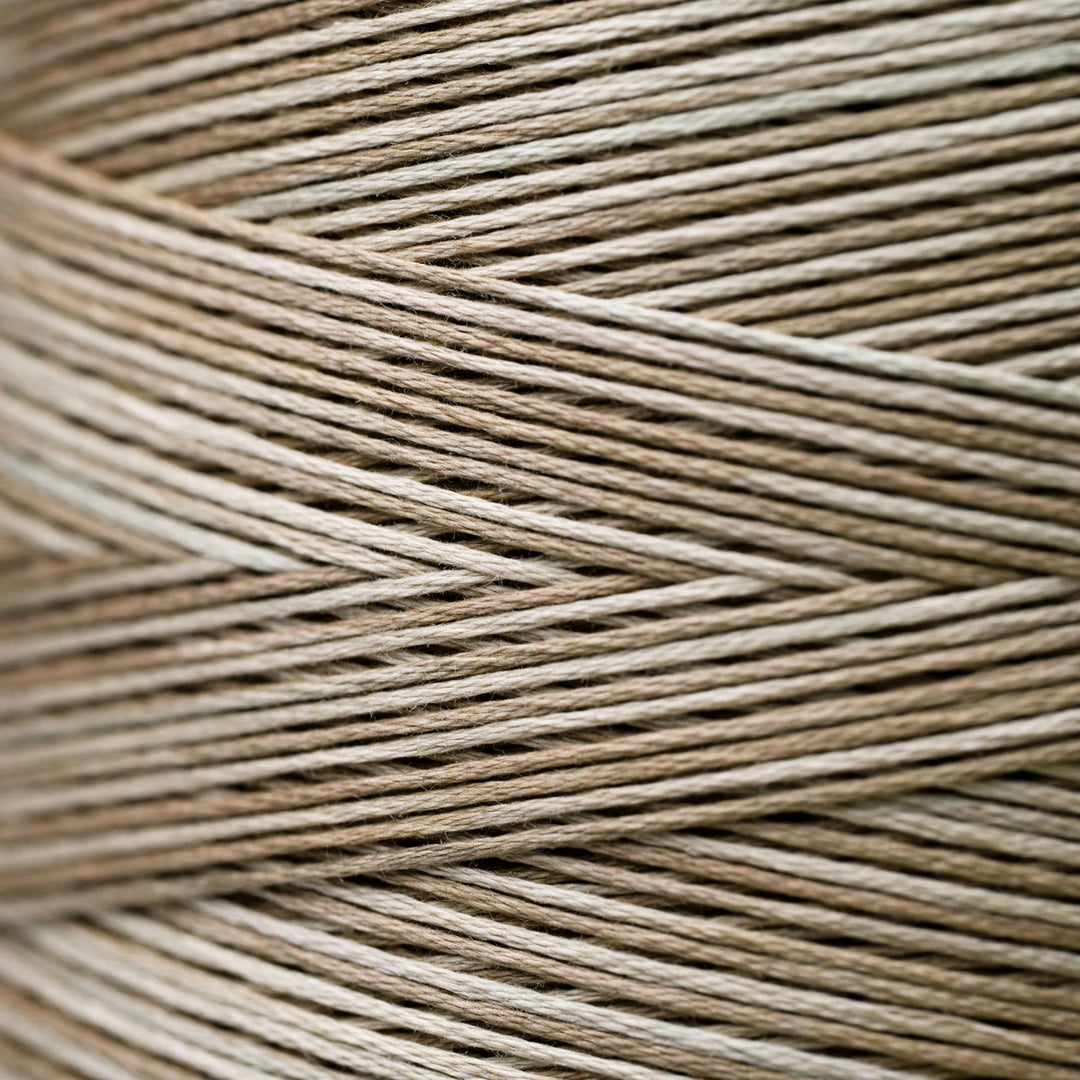 A close-up texture shot of braided twine or cord in a variegated light brown and beige color, arranged in a herringbone pattern.
