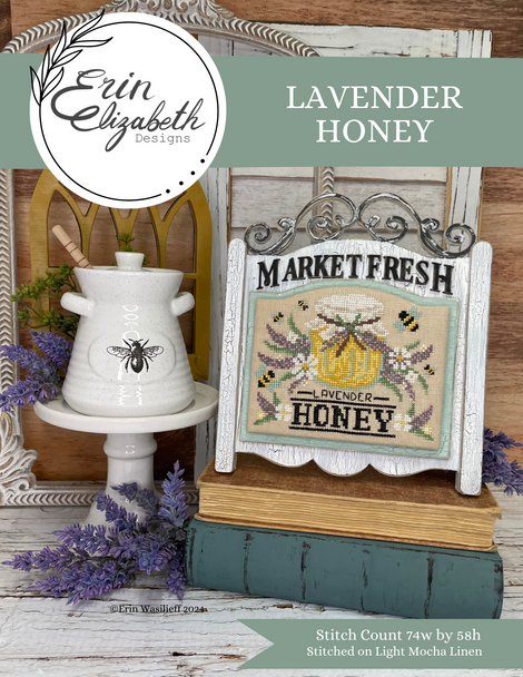 Erin Elizabeth Designs lavender honey cross stitch kit with a white bee-themed candle and framed text on a wooden surface.