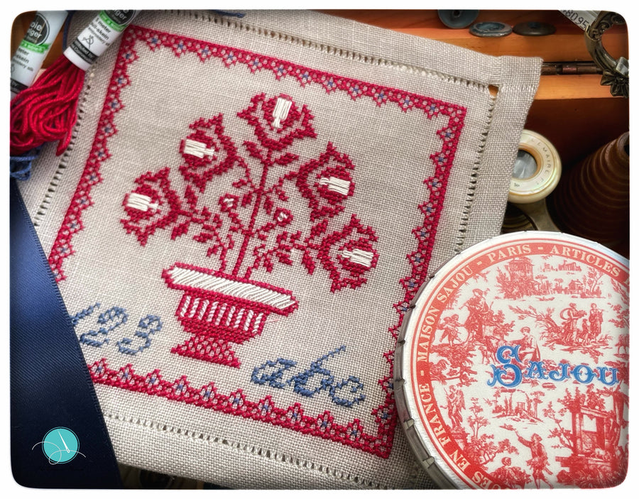 Embroidered fabric with floral design and 'Sazou' branding, surrounded by sewing materials.