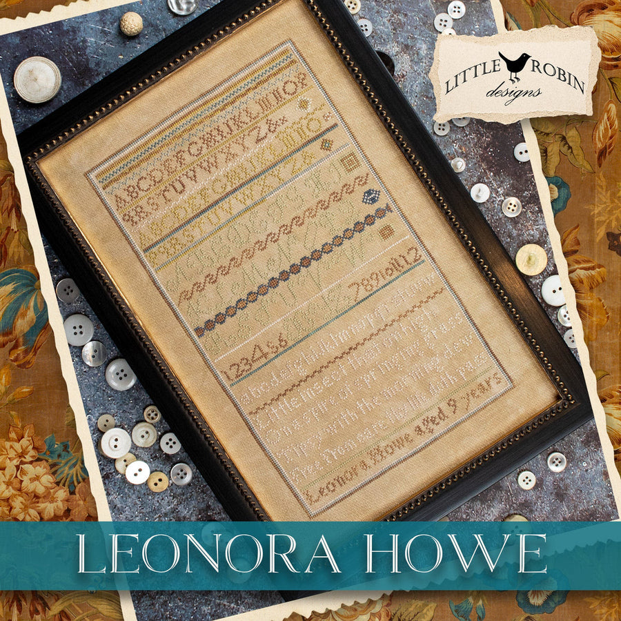 A framed Leonora Howe sampler artwork shown at an angle on a decorative fabric background with buttons and paper trim. The sampler features embroidered alphabet rows, decorative borders, and text.