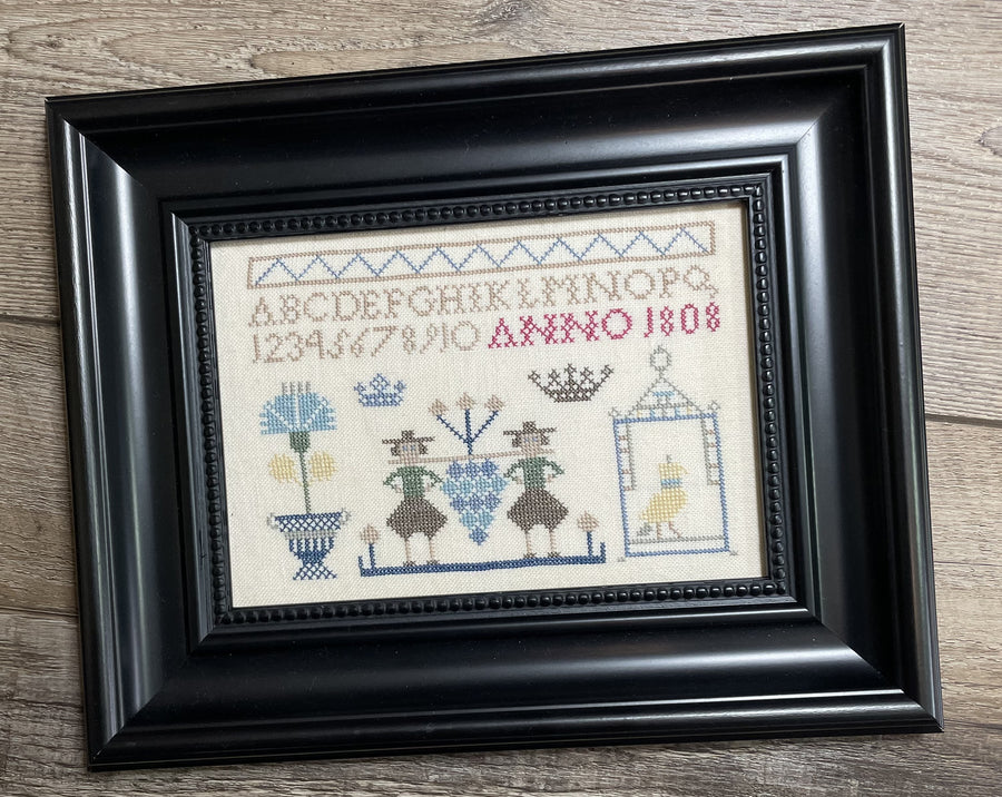 Framed cross-stitched sampler with decorative elements on a wooden surface