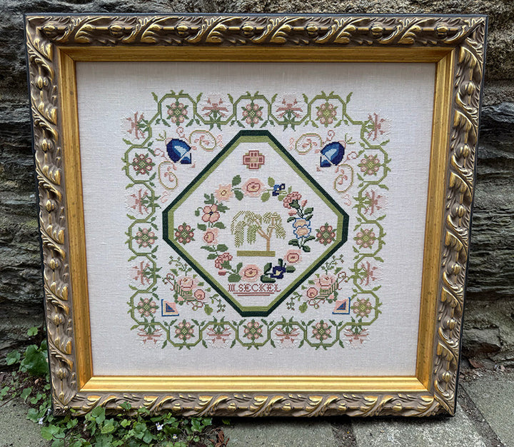 Framed cross-stitched piece with decorative border on a stone surface