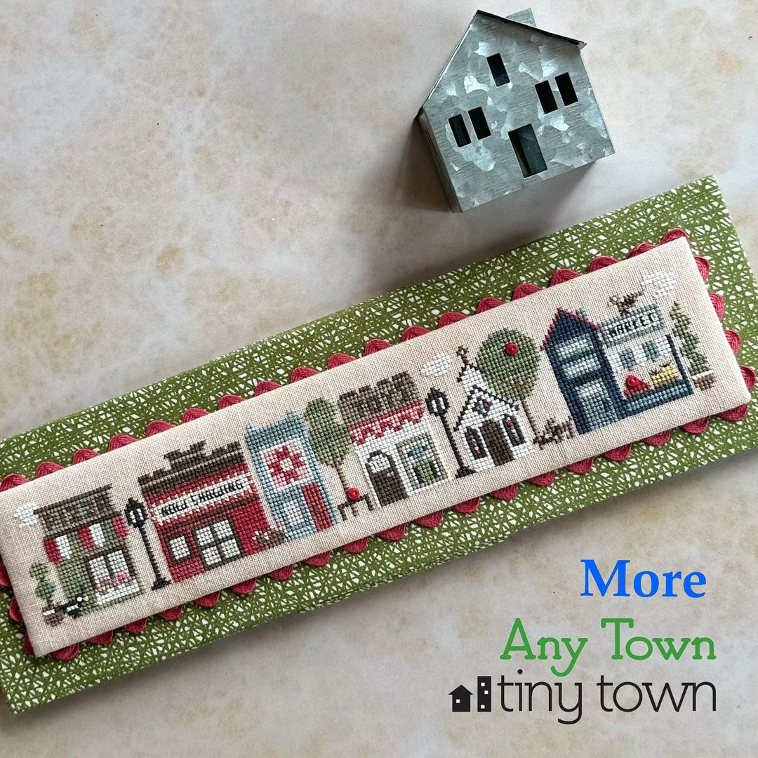 Cross-stitched bookmark with town scene on a green ribbon, with 'Tiny Town' branding.