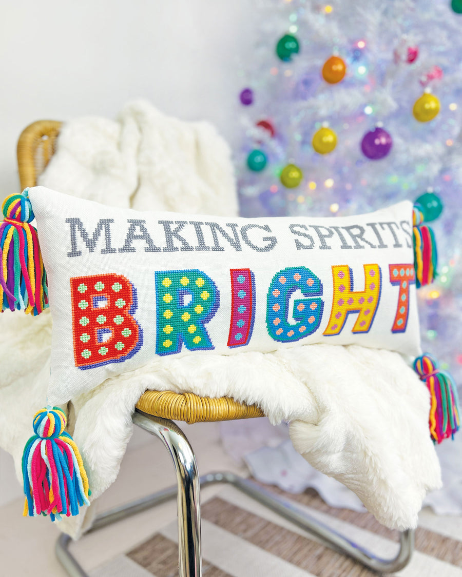 Decorative pillow with colorful text 'MAKING SPIRITS BRIGHT' on a chair with a festive background.