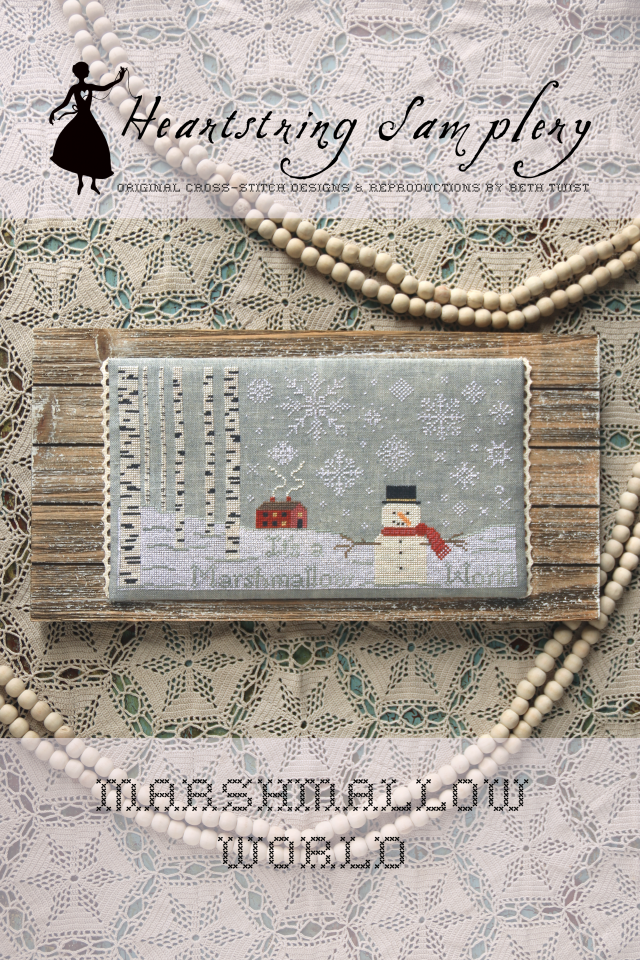 Heartstring Samplery 'Marshmallow World' cross-stitch pattern with wooden frame and snowman design on textured fabric.