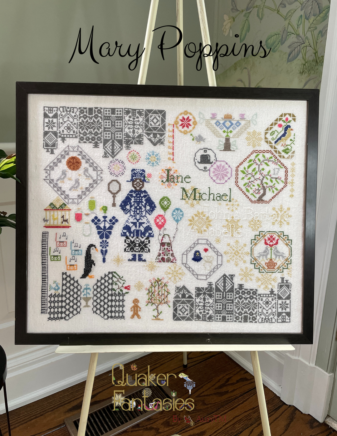 Framed cross-stitch pattern with 'Jane Michael' and decorative elements on a stand.