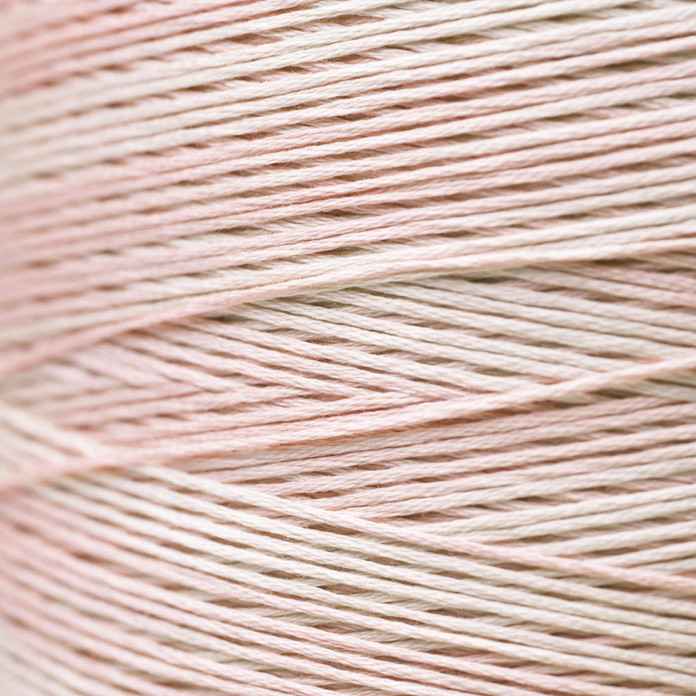 A close-up of fine thread strands wound horizontally, showing a soft pastel color blend of pale pink and warm off-white.