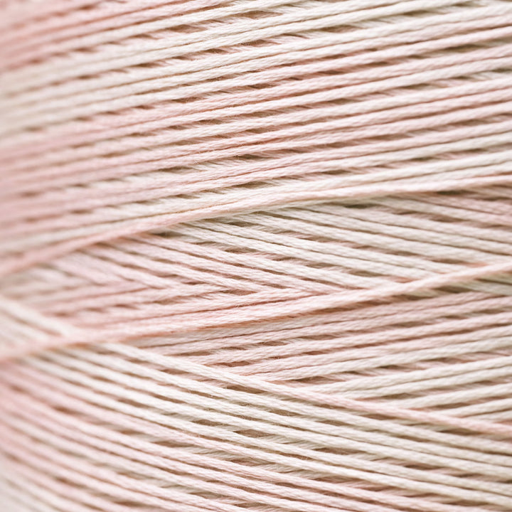 A close-up of fine thread strands wound horizontally, showing a soft pastel color blend of pale pink and warm off-white.