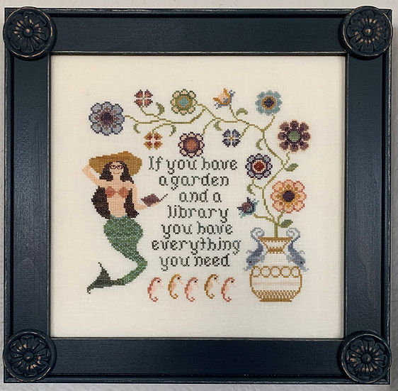 Cross-stitched design with mermaid, flowers, and text in a black frame.