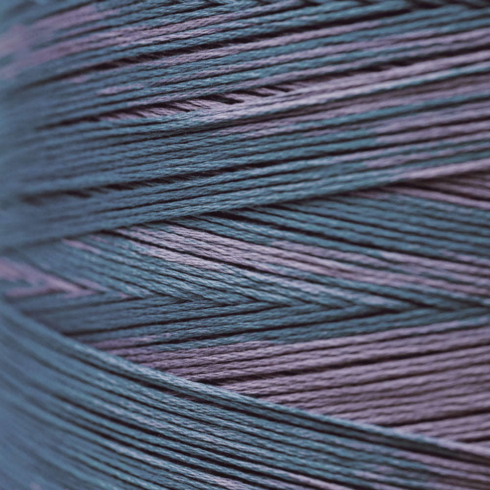 A close-up of tightly wound yarn strands in a heathered blend of muted teal-blue and dusty lavender-purple.