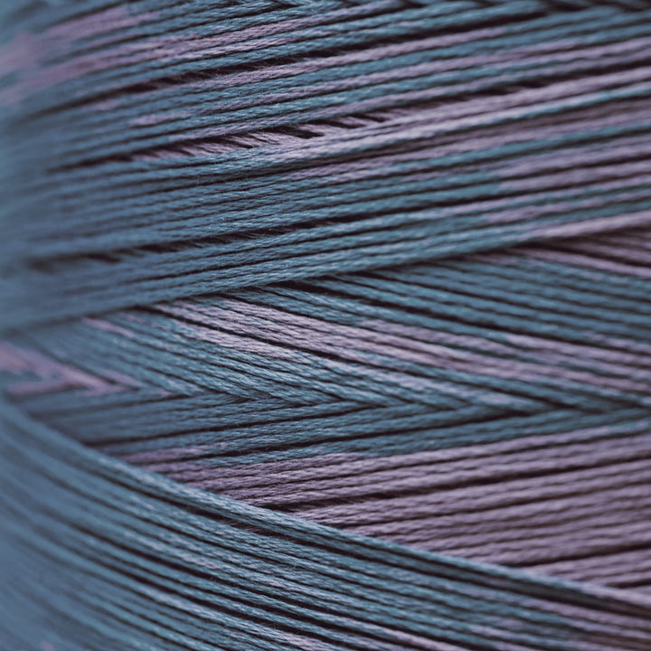 A close-up of tightly wound yarn strands in a heathered blend of muted teal-blue and dusty lavender-purple.