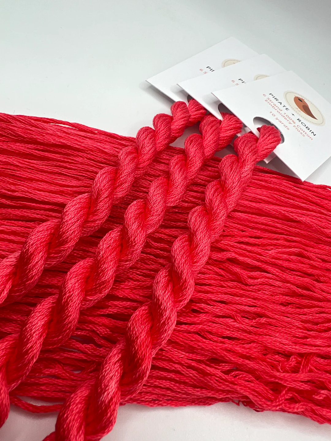 Red embroidery floss  with a packaging of knitting needles on a light gray background