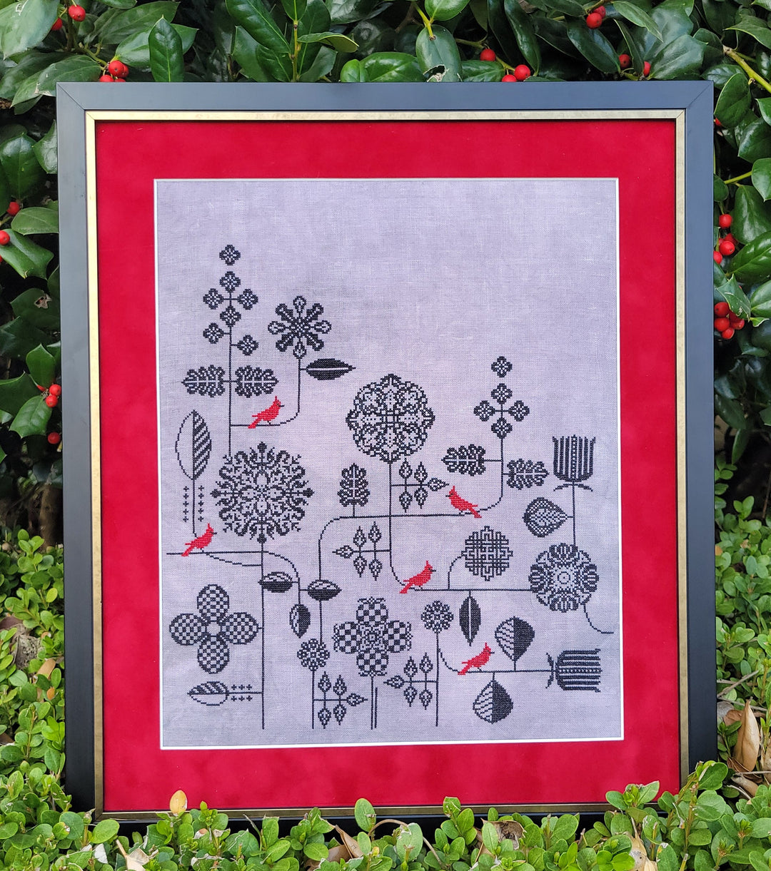 Framed black floral pattern on gray fabric with red border against a green leafy background