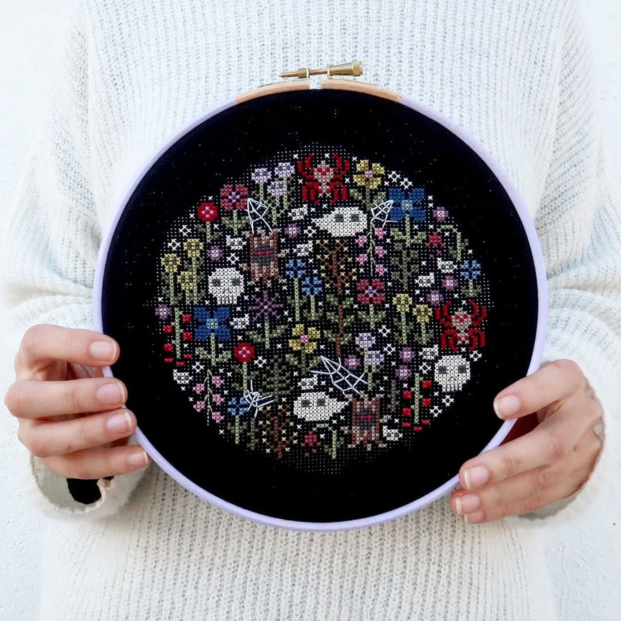 Person holding a cross-stitched piece of art on a black background