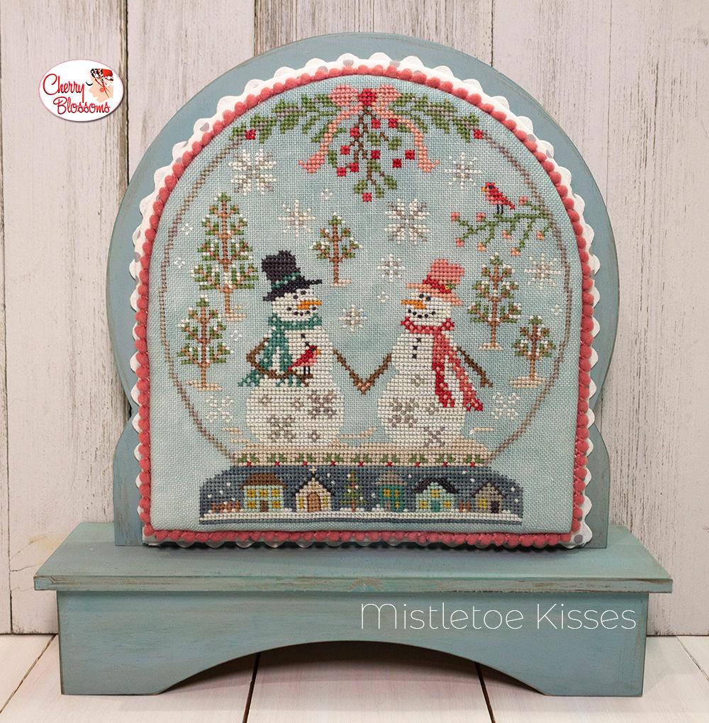 A cross-stitching kit depicting a winter scene with a snowman, snowflakes, and Christmas decorations, framed in a snowglobe-like structure.