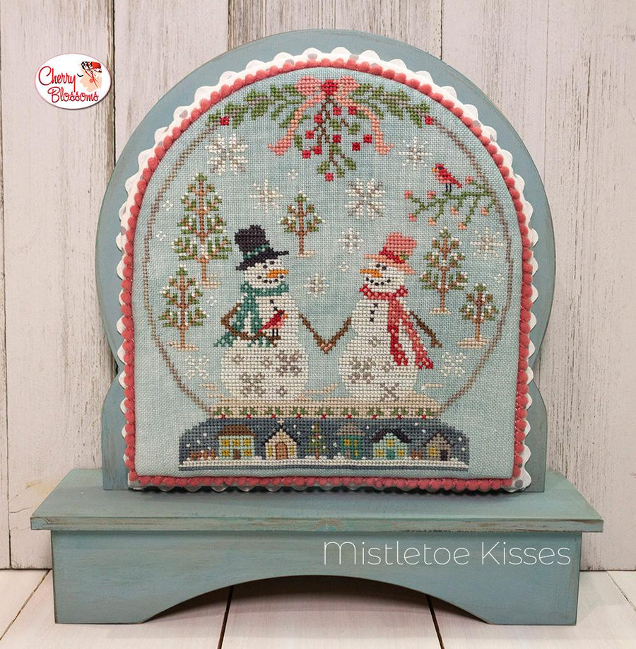 A cross-stitching kit depicting a winter scene with a snowman, snowflakes, and Christmas decorations, framed in a snowglobe-like structure.