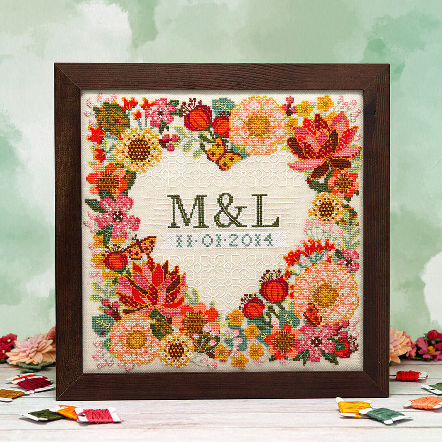 Framed cross-stitched artwork with floral design and initials 'M&L' on a light background