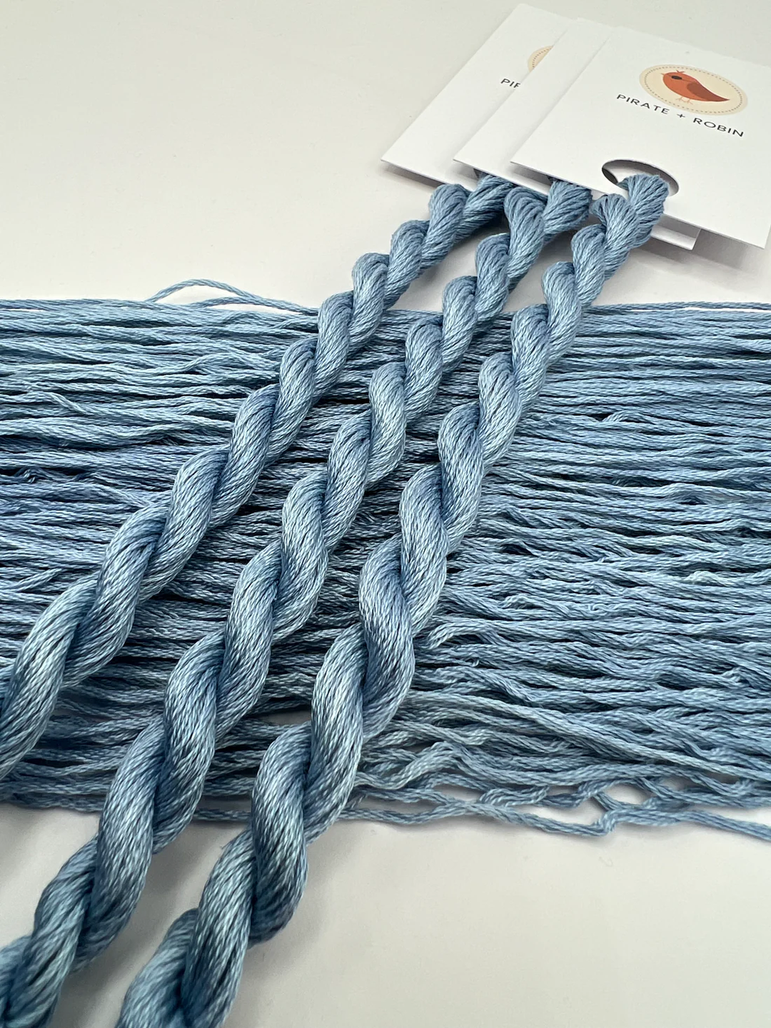 Blue thread skeins on a white surface with a brand label in the background.