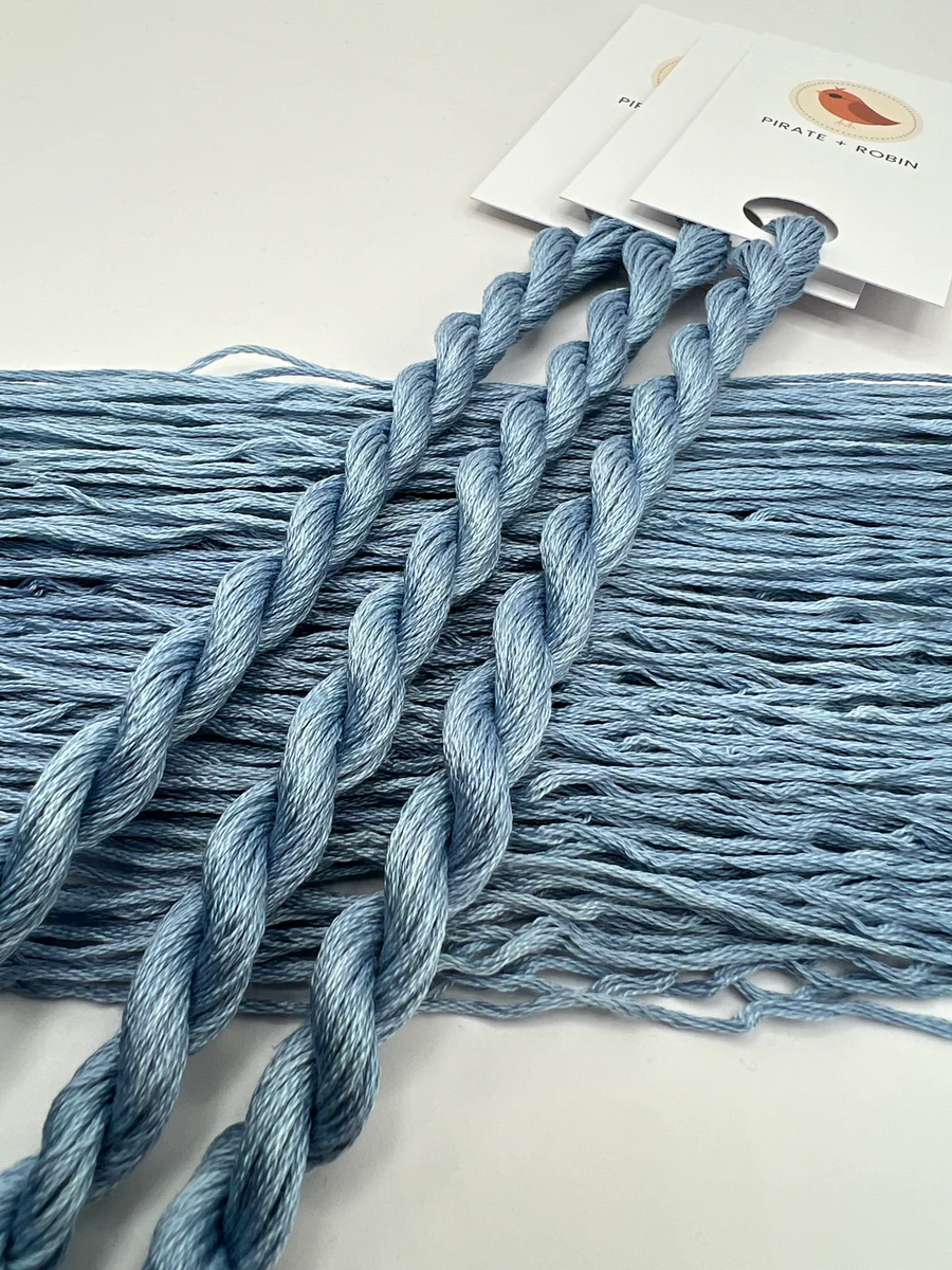 Blue thread skeins on a white surface with a brand label in the background.