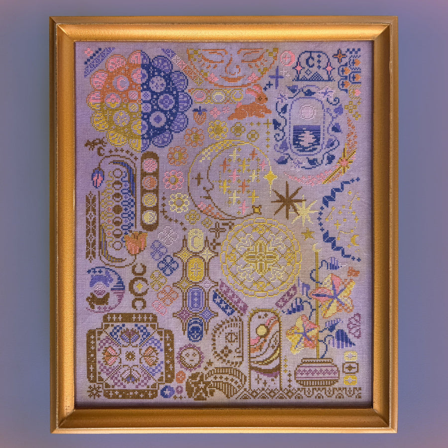 A framed decorative needlepoint or embroidered artwork featuring an intricate multicolor pattern with geometric and floral motifs, enclosed in a gold-toned frame against a solid purple background.