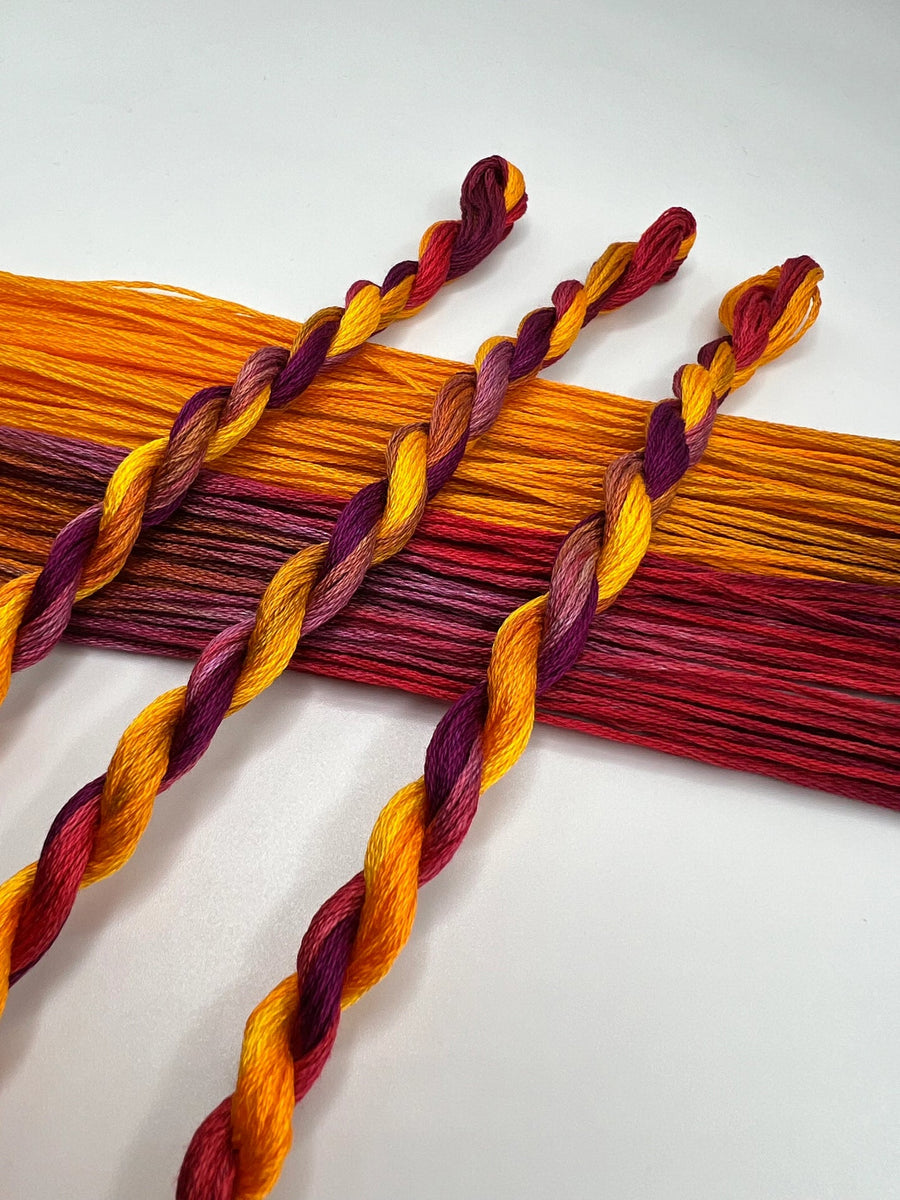 Braided thread skeins in orange, red, and purple on a white background