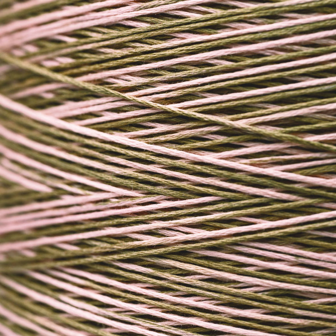 A close-up of tightly wound embroidery thread in a variegated colorway of olive green, dusty pink, and light brown.