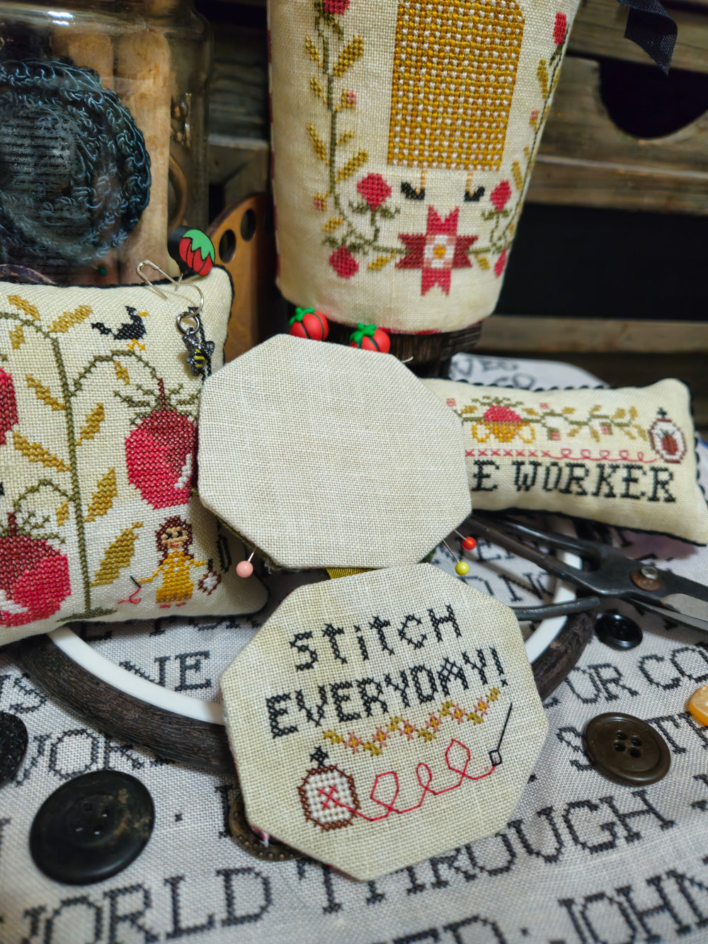 Decorative cross-stitched items with text and patterns on a surface with sewing tools.