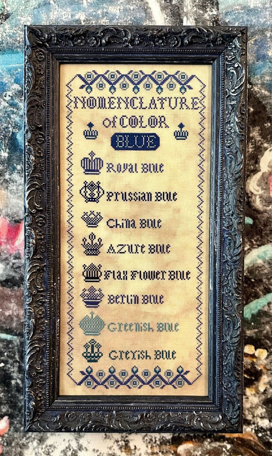 Cross stitch kit cover for 'Nomenclature of Color - Blue' with a list of royal and regal blue patterns stitched in a decorative font.