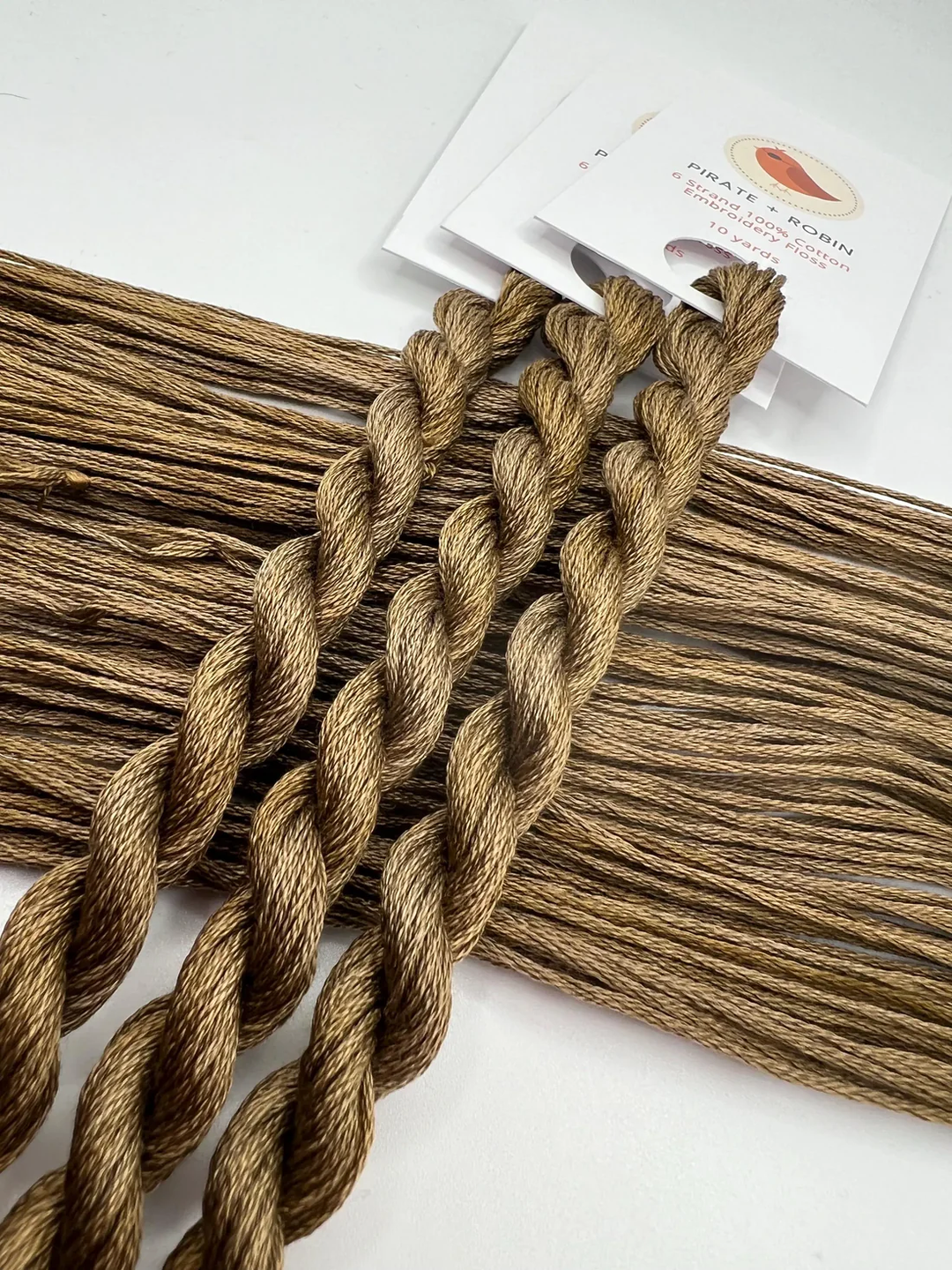 Brown braided embroidery floss skeins on a white background with a brand card.