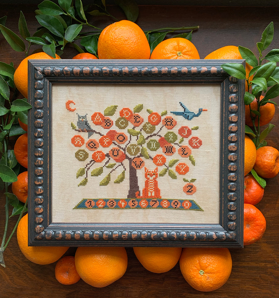 Framed cross-stitched tree with animals surrounded by oranges