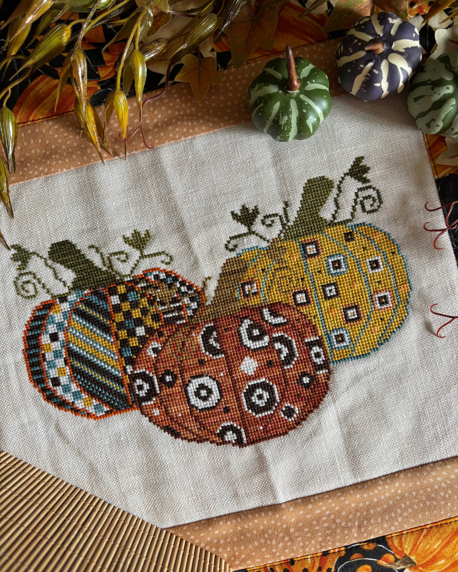 Cross-stitched pumpkins on fabric with a textured surface
