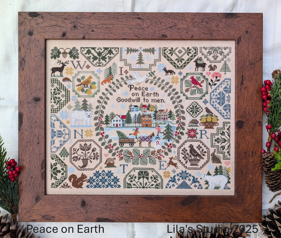 Framed cross-stitched sampler with 'Peace on Earth' text and festive elements, Lila's Studio branding visible.