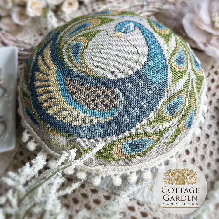 Decorative pillow with peacock feather pattern on a textured surface, featuring the Cottage Garden Samplings logo.