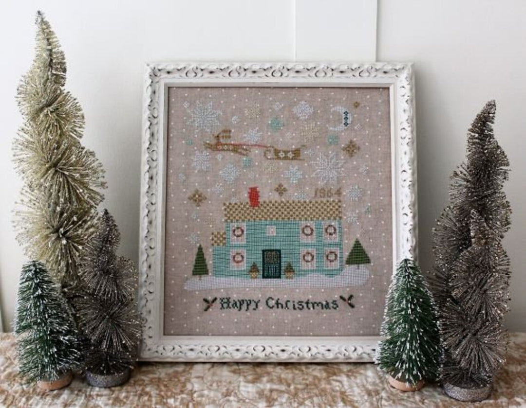 Framed cross-stitched Christmas scene with decorative trees on a textured surface.