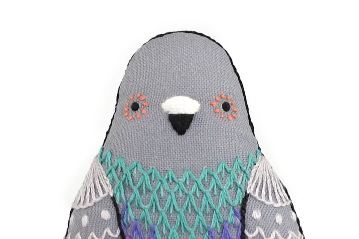 Stuffed toy penguin with gray body, teal patterned wings, and white face on a white background