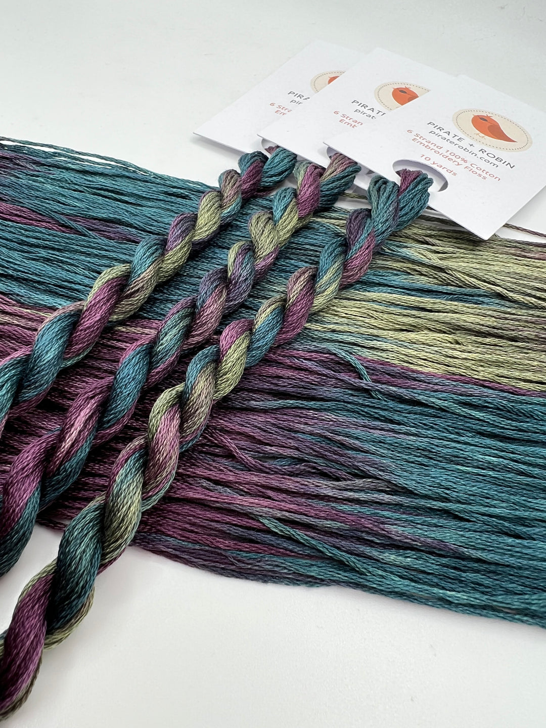 skeins of purple blue green thread with a brand label in the background