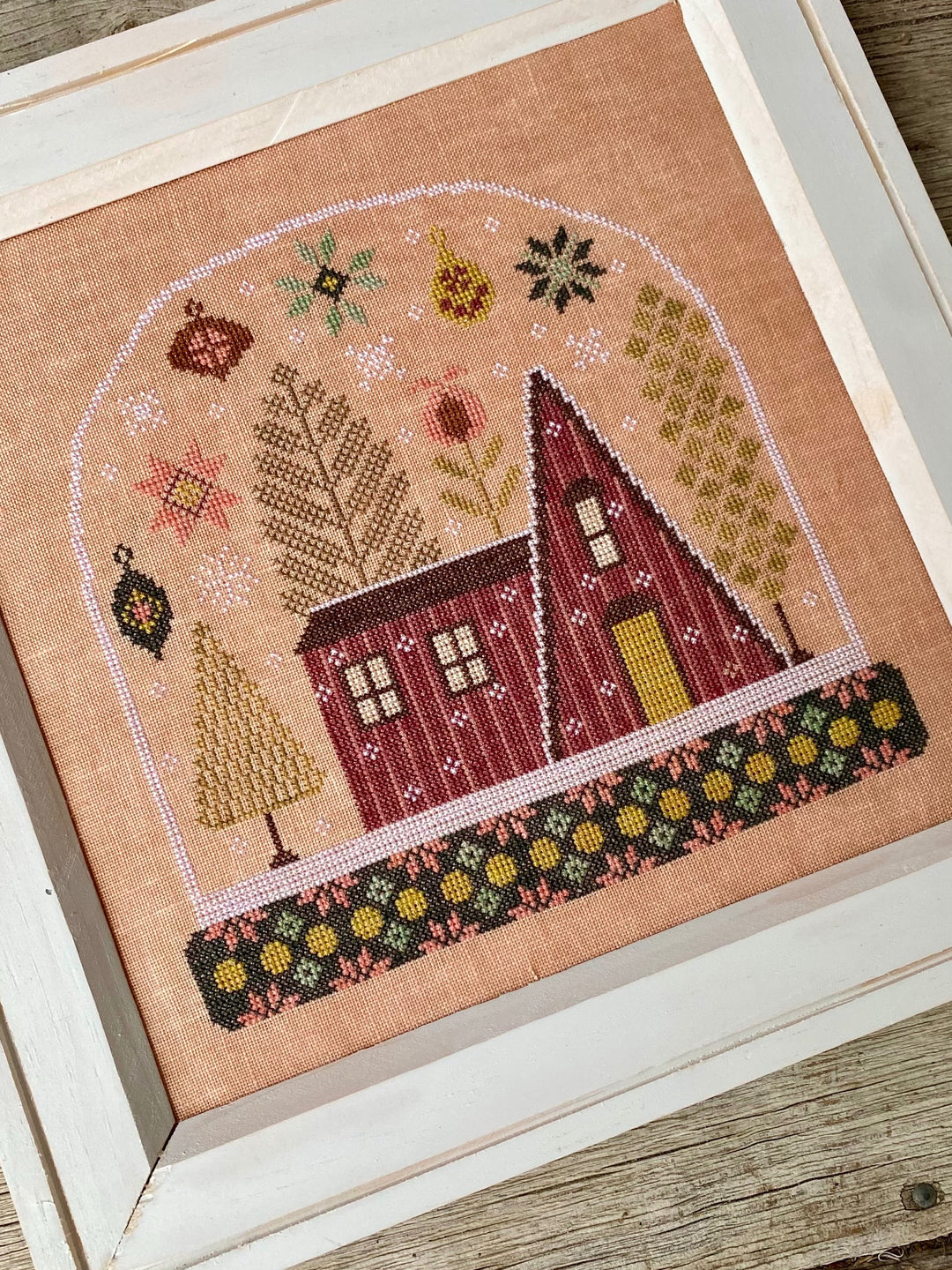 Cross-stitched house on fabric with a wooden frame