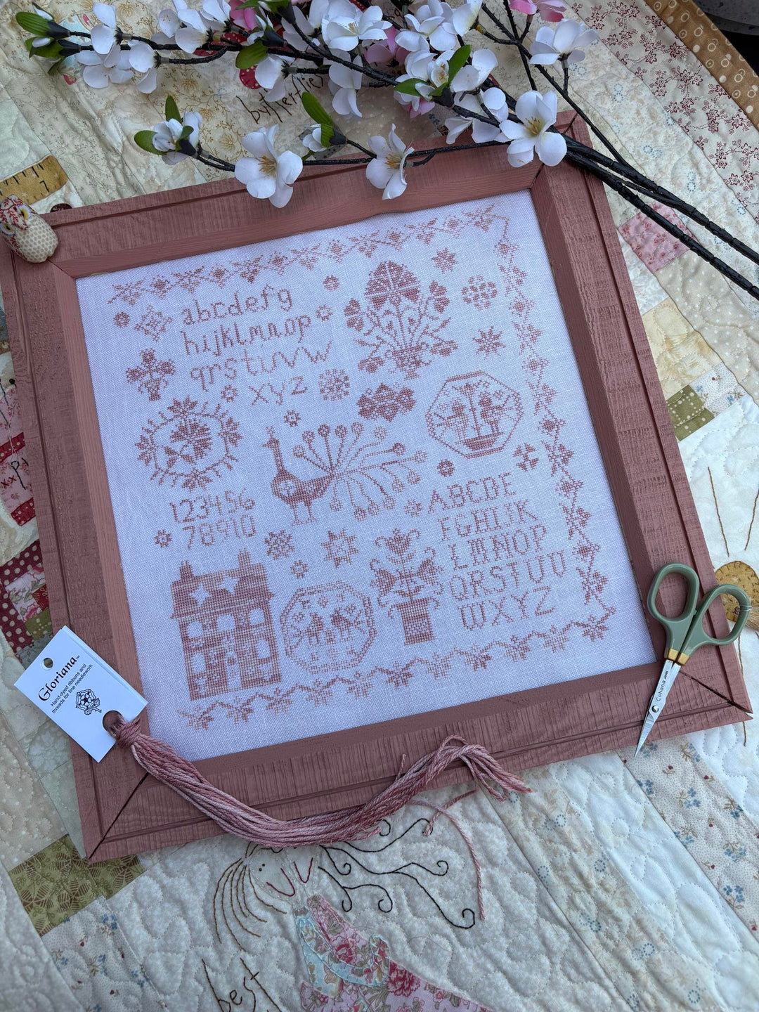 Framed cross-stitched sampler with floral decorations on a quilted surface.
