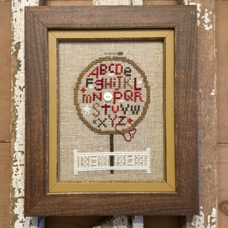 Cross-stitched heart design in a wooden frame with text about a stitching kit.