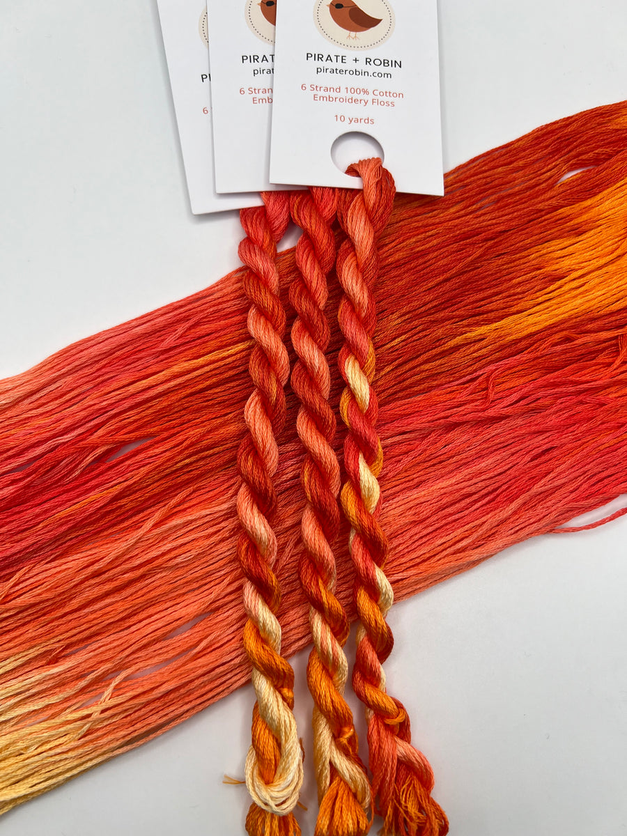 Braided yarn with orange and red tones on a white background, featuring a brand label.