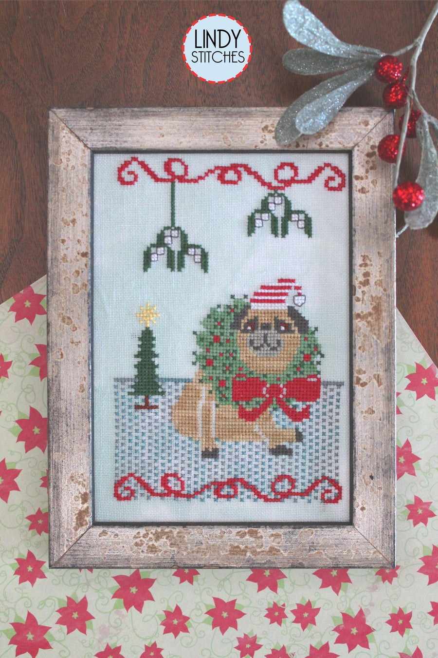 Cross-stitched design of a dog with a Christmas wreath, framed and surrounded by festive elements.