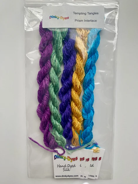 A clear plastic bag containing five twisted thread skeins in purple, mint green, yellow, and blue, labeled 'Tempting Tangles Prism Interface' by Pinky Dyes.
