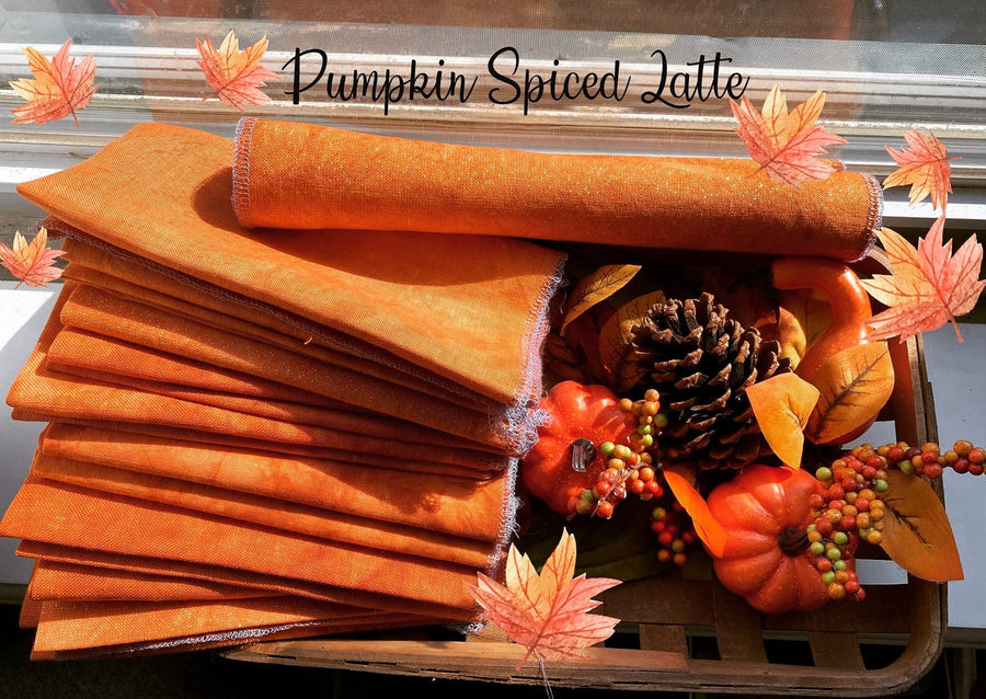 A stack of orange-brown fabric sits in a wooden tray beside autumn-themed decorations, including a pinecone, small pumpkins, berries, and fall leaves. The words 'Pumpkin Spiced Latte' appear across the top as a decorative text overlay.