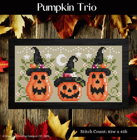 A framed cross-stitch design titled 'Pumpkin Trio' showing three orange jack-o'-lantern pumpkins wearing black witch hats, arranged on a rustic wooden background with autumn leaves. Text at the top reads 'Pumpkin Trio,' and a bottom label notes stitch count 83w x 43h.