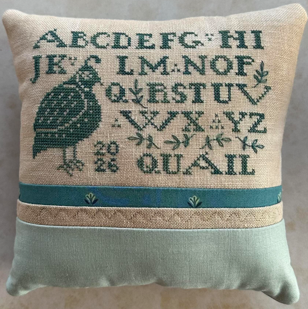 Quail Sampler pillow with cross-stitch pattern on a plain background