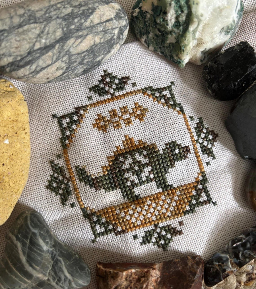 Cross-stitched design of a stegosaurus surrounded by decorative stones on fabric